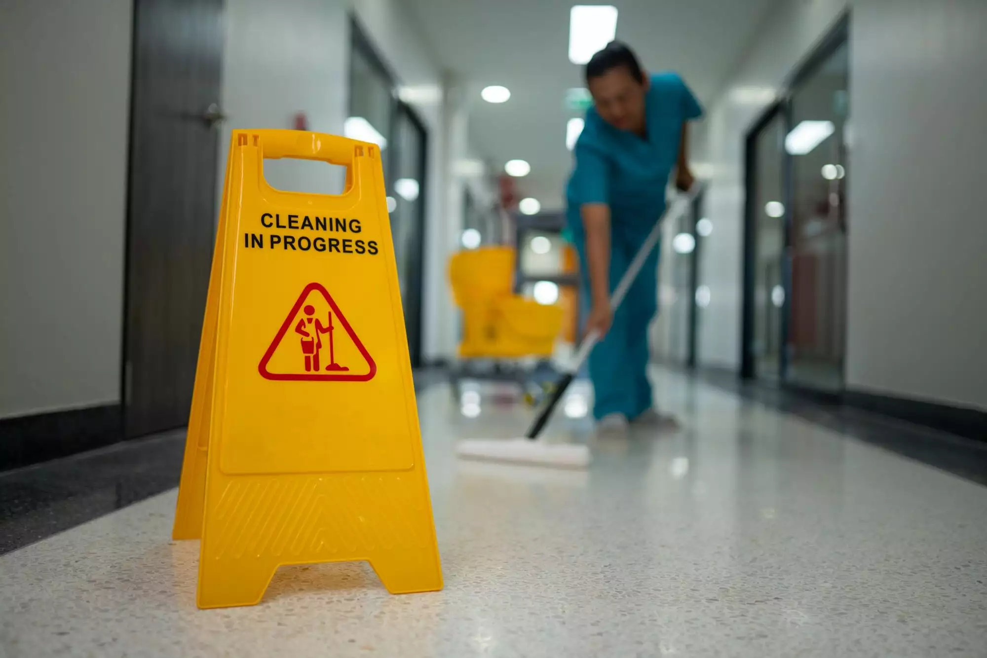 A woman is cleaning a floor with a yellow sign that says 