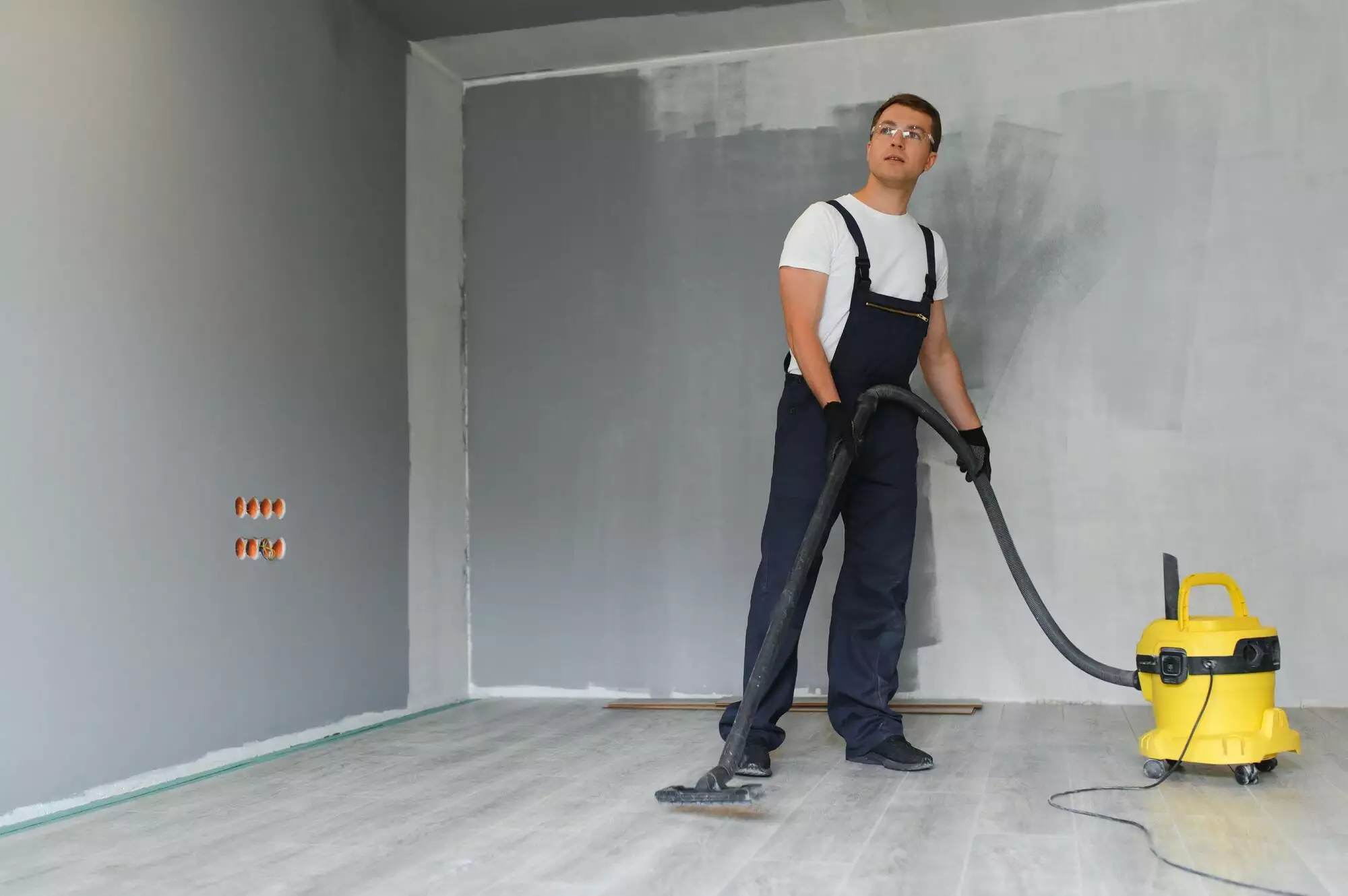 male worker in overall vacuum cleaning during apartment renovation