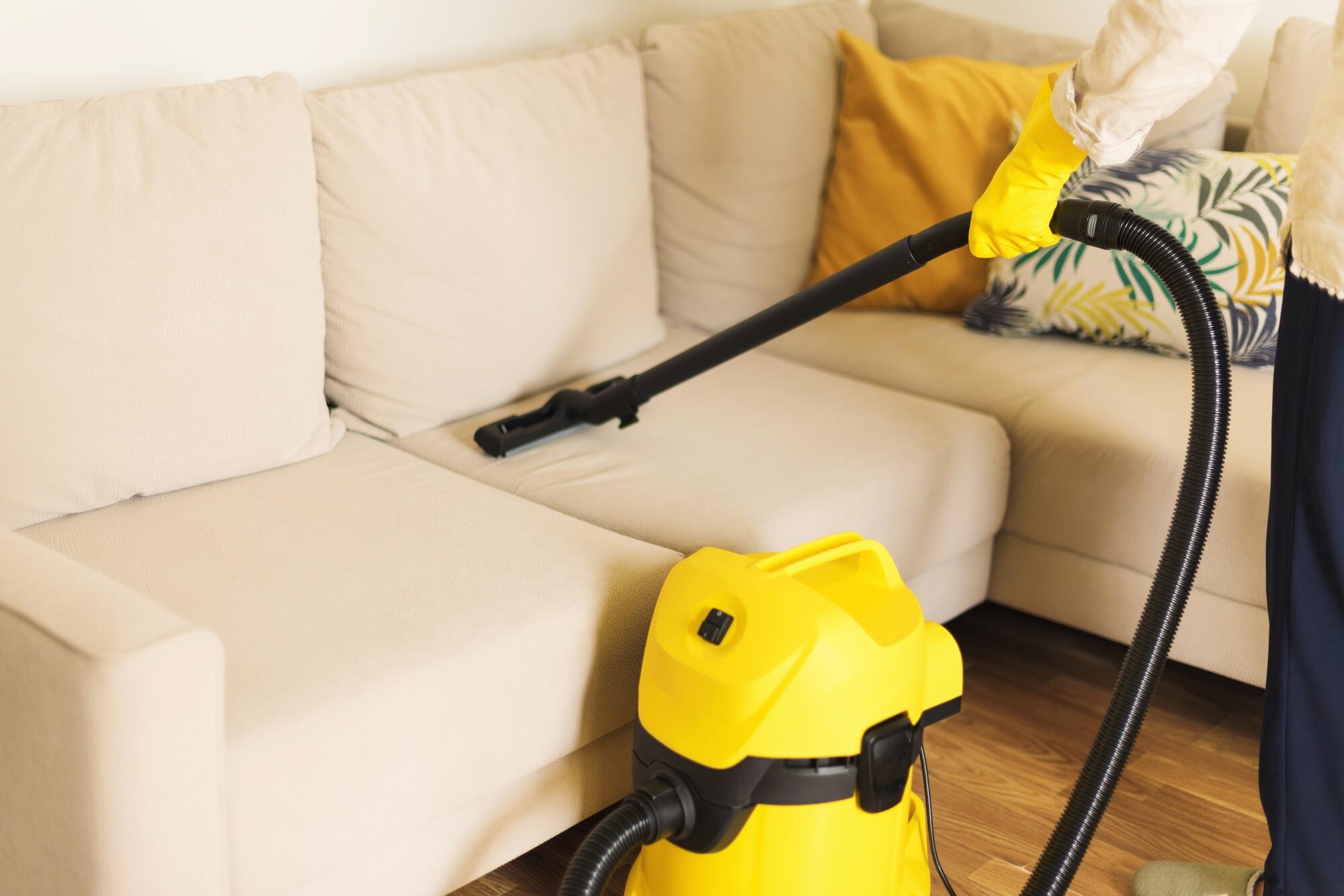 Woman cleaning sofa with yellow vacuum cleaner. Copy space. Clean concept