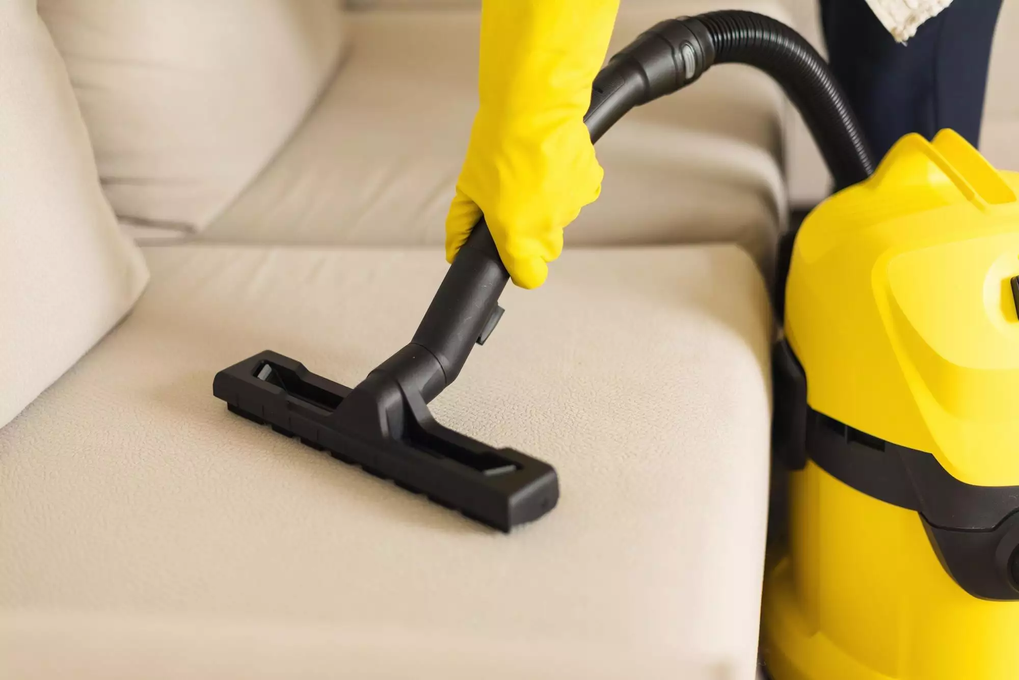 Woman cleaning sofa with yellow vacuum cleaner. Copy space. Clean concept